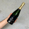 Hand holding a bottle of Abele champagne against a gray background