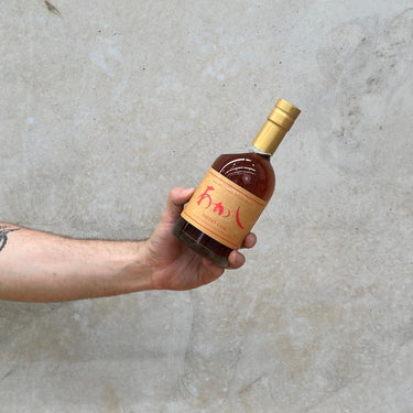 A hand holding a bottle of Eigashima Akashi 5 Year Old Sherry Cask Whisky with a concrete background.