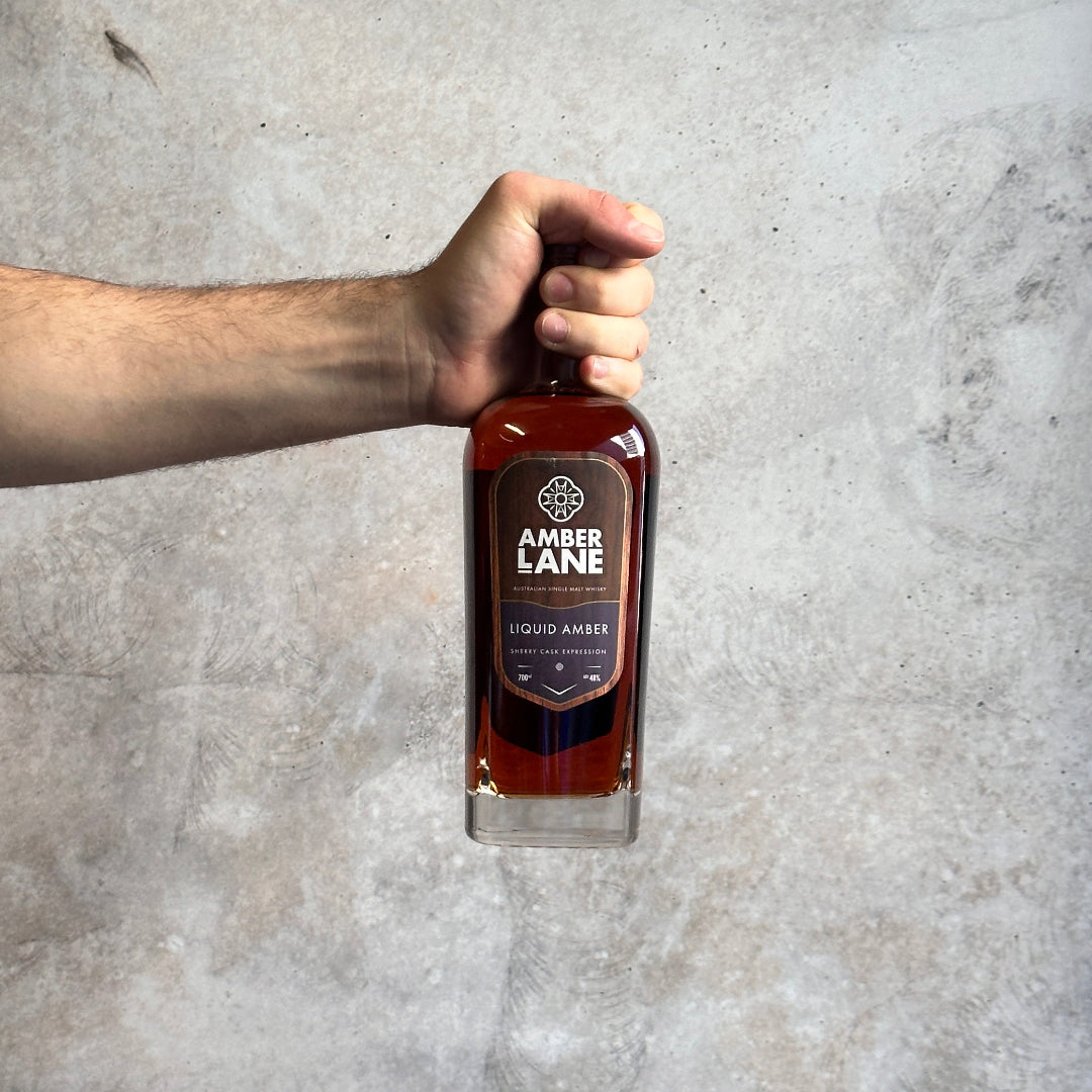 Hand holding a bottle of Amber Lane Liquid Amber against a gray concrete background