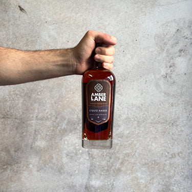 Hand holding a bottle of Amber Lane Liquid Amber against a gray concrete background