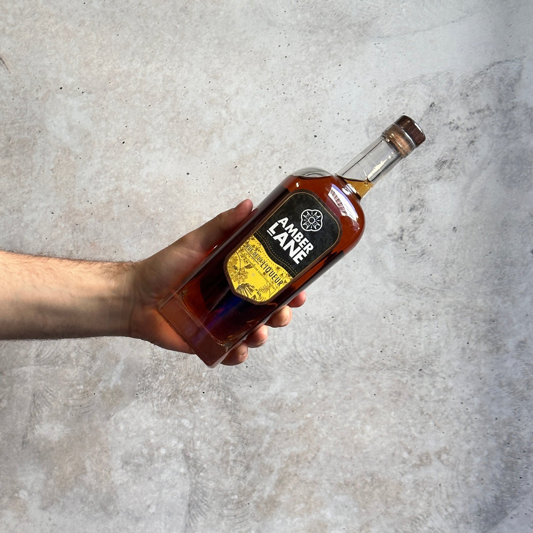 Hand holding a bottle of Amber Lane whiskey against a gray concrete background