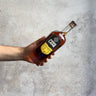 Hand holding a bottle of Amber Lane whiskey against a gray concrete background
