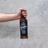 A hand holding a bottle of Amrut Portonova Whisky with a concrete wall in the background.