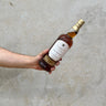 A hand holding a bottle of Amrut Single Cask #3897 Oloroso Cask Whisky against a grey concrete background.
