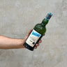 A hand holding a bottle of Ardbeg Ardcore Committee Release Whisky with a concrete background.