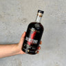Bottle of Balcones Brimstone corn whiskey held by a hand against a gray background