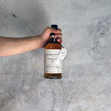 Hand holding a bottle of Balvenie whisky aged 25 Years against a gray concrete background