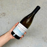 Hand holding a white wine bottle with a label against a gray background