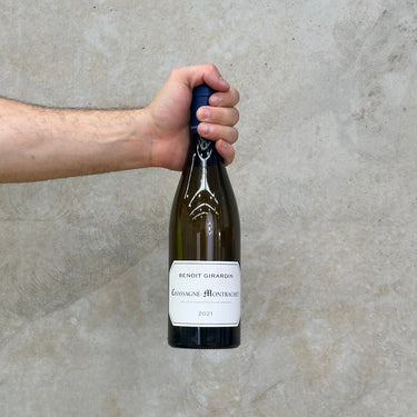 A hand holding a bottle of Benoit Girardin 2021 Chassagne Montrachet white Burgundy wine