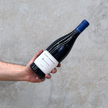 A hand holding a bottle of Benoit Girardin 2021 Santenay red wine, with a concrete background.