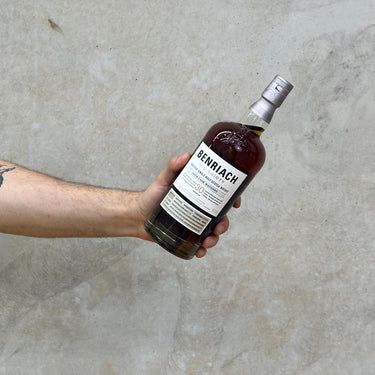 A hand holding a bottle of Benriach 30 Year Old Whisky against a grey textured background.