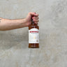 A hand holding a bottle of Benromach 21 Year Old single malt Scotch whisky against a grey textured background.