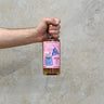 A hand holding a bottle of That Boutique-y Whisky Company Aberlour 31 Year Old whisky with a pink label, against a grey concrete background.