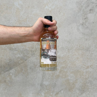 A hand holding a bottle of Longmorn 10 Year Old single malt whisky with a label that includes a picture of the distillery and some fruits.
