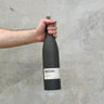 A hand holding a bottle of Bozal Castilla Ancestral Mezcal against a grey background.
