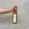 A hand holding a bottle of Brora 34 Year Old Scotch Whisky against a grey textured background.