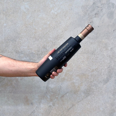 A hand holding a bottle of Bruichladdich Octomore 8.1 Whisky with a concrete background.