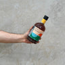 A hand holding a bottle of Bruichladdich Rock'n'Daal 1.2 Whisky with a concrete background.