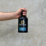 A hand holding a bottle of Bunnahabhain 18 Year Old Whisky against a grey concrete background.