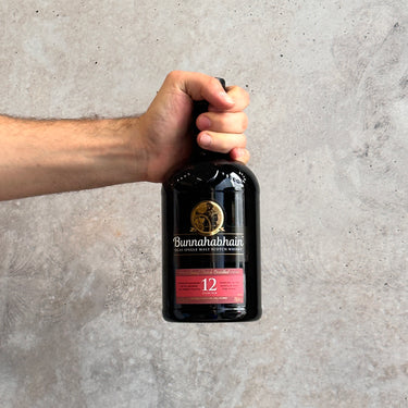 Hand holding a Bunnahabhain whisky bottle Aged 12 Years against a gray background