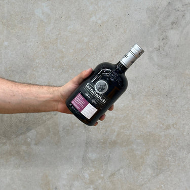 A hand holding a bottle of Bunnahabhain 2011 Aonadh 10 Year Old Port & Sherry Cask Scotch whisky against a grey concrete background.