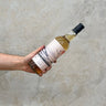 A hand holding a bottle of Ledaig 15 Year Old Cantina/Aqauvitae Bottling Whisky against a grey concrete background.