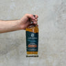 Hand holding a bottle of Cape Byron Australian Single Malt Whisky against a neutral background