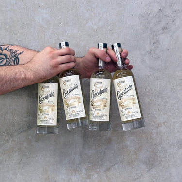 Four bottles of Cacapulco tequila held by a person against a gray concrete background
