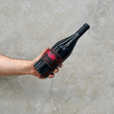 A hand holding a bottle of Chétaito Revelette wine with a black label on a textured grey background.