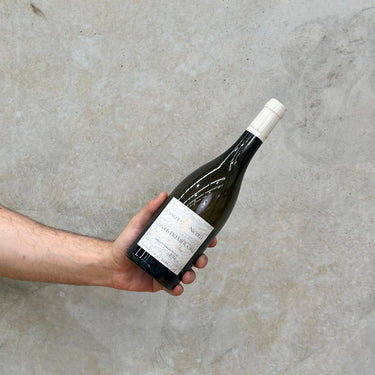 A hand holding a bottle of Charly Nicolle Chablis 1er Cru Mont De Milieu against a concrete background.