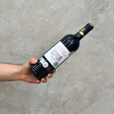A hand holding a bottle of 2019 Chateau Saint-Yzans Medoc wine against a concrete background.
