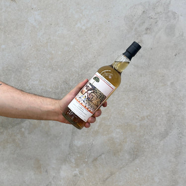 A hand holding a bottle of Tullibardine Chorlton 29 Year Old Whisky with a concrete surface in the background.