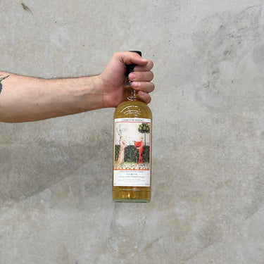 Hand holding a bottle of Chorlton Whisky against a gray concrete wall