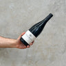 A hand holding a bottle of Florent Descombe 2018 Côte - Rôtie wine against a grey concrete background.