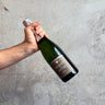 Hand holding a bottle of Cremant de Savoie Champagne Sparkling Wine against a gray concrete background