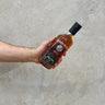 Hand holding a bottle of Darknes whiskey against a concrete wall.