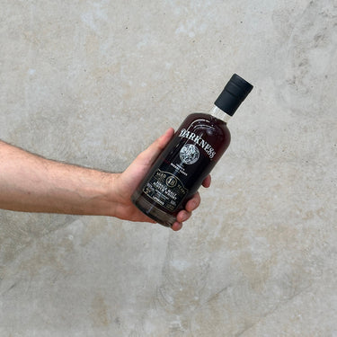 A hand holding a bottle of Laphroaig Darkness 18 Year Old Pedro Ximenez Cask whisky against a textured grey background.