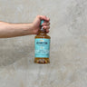 A hand holding a bottle of Deanston 15 Year Old Tequila Cask Whisky with a grey background.