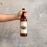 Hand holding a bottle of Decadent Drams Whisky against a gray concrete background