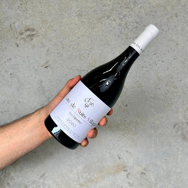 Hand holding a bottle of wine labeled 'Cote de Nuits Villages' against a gray background
