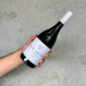 Hand holding a bottle of wine labeled 'Cote de Nuits Villages' against a gray background