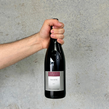 Hand holding a bottle of Domaine Berthaud Cairanne wine against a gray background