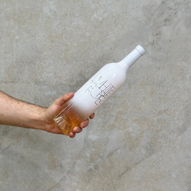 A hand holding a bottle of Domaine Tropez 2021 White Tropez Rosé with a concrete background.
