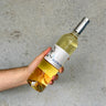 Hand holding a bottle of Sauvignon White wine with a label against a gray background