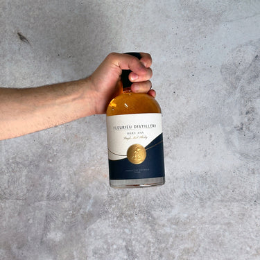 Hand holding a bottle of Fleurieu Distillery Mary Ann Whisky against a gray background