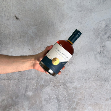 Hand holding a bottle of Fleurieu Whisky with a label against a gray concrete background