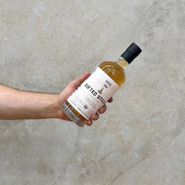 A hand holding a bottle of Arran Jean Boyer Gifted Stills Of Scotland 1996 Whisky against a grey concrete background.