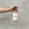A hand holding a bottle of Benriach Jean Boyer Gifted Stills Of Scotland 2012 Whisky against a grey concrete background.