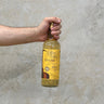 A hand holding a bottle of Tomatin Jean Boyer Gifted Stills Of Scotland 2008 Whisky with a yellow label.