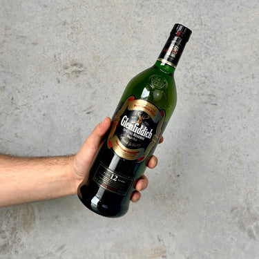 Hand holding a bottle of Glenfiddich Special Reserve Agef 12 years whisky against a gray background